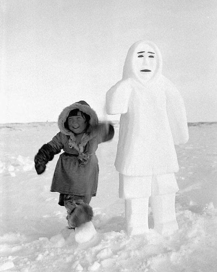 Child smiling next to a snow sculpture, showcasing a forgotten corner of history.