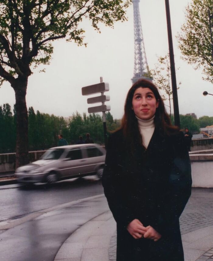 A woman stands on a Paris street by the Eiffel Tower, representing forgotten corners of history.