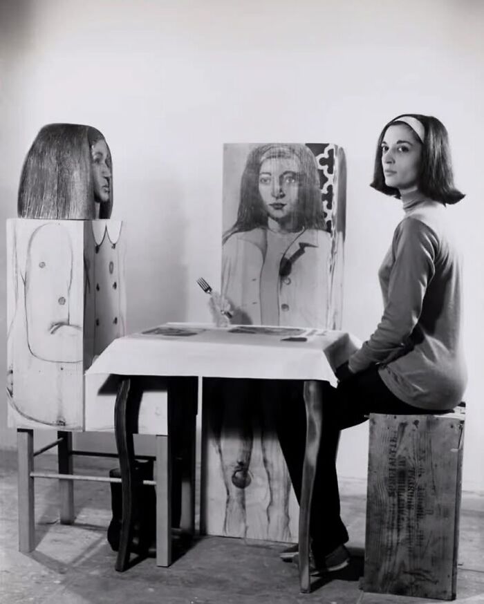 Woman seated at a table with painted wooden figures, evoking forgotten corners of history.