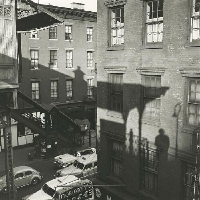 Shadows on brick buildings and vintage cars in an urban scene capture forgotten corners of history.