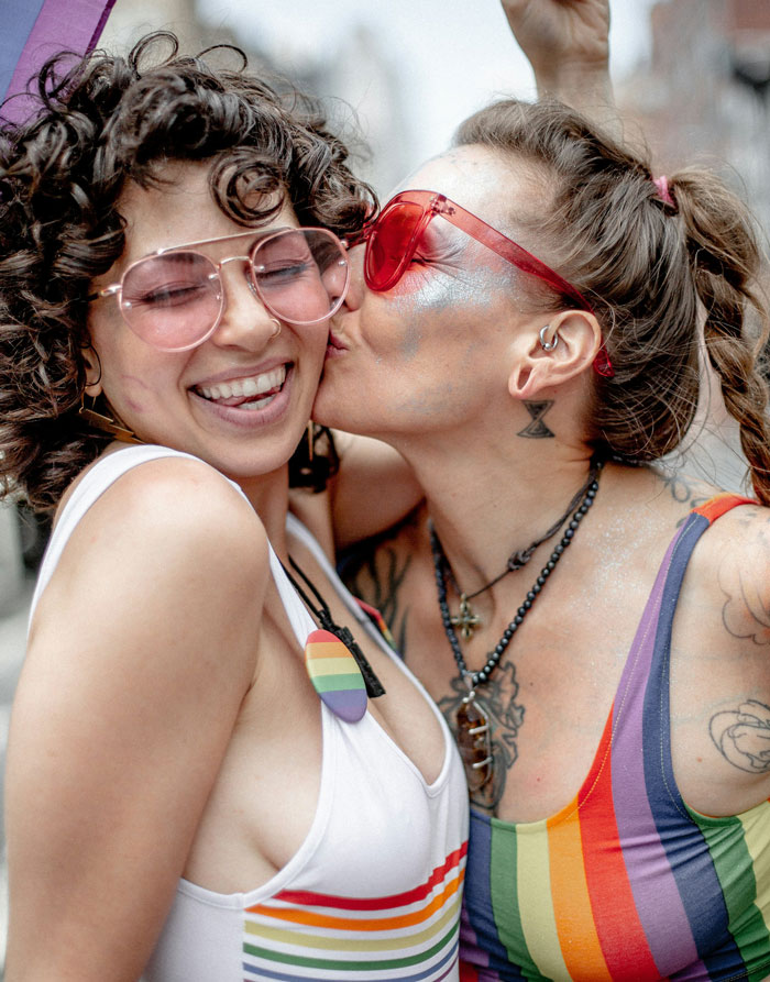 Two women in pride-themed outfits sharing a joyful moment, embodying a vibrant and supportive atmosphere.