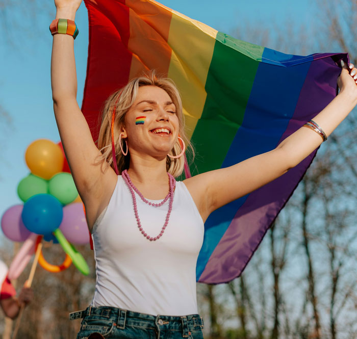 Woman celebrating pride with a rainbow flag, smiling outdoors.