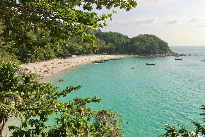 Stunning beach with turquoise waters, surrounded by greenery and boats, inviting a tropical getaway.