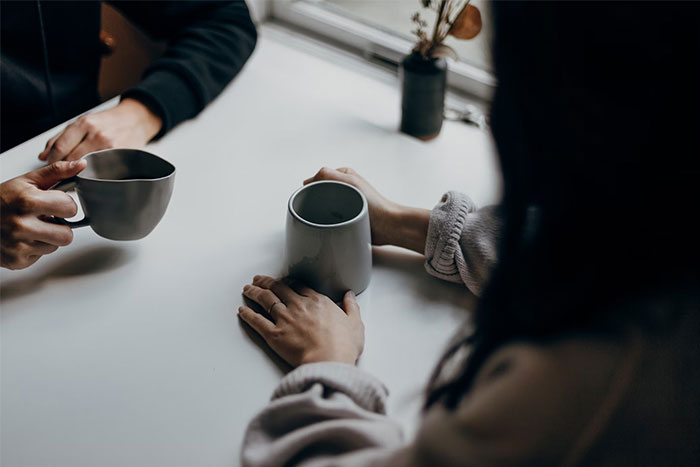 Two people holding mugs across a table, capturing a moment of dating interaction.