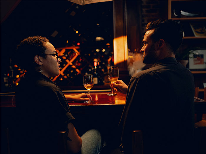 A woman and a man on a date at a dimly lit bar, holding wine glasses, engaging in conversation.