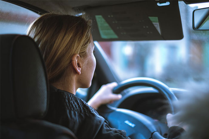 A woman driving a car, seen from behind, focusing on the road ahead.