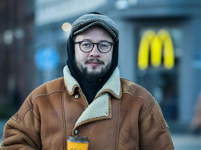 Man in glasses and brown coat holds a coffee cup outside a fast-food restaurant, representing creepy dating experiences.