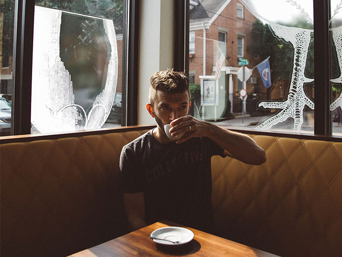 Man sitting alone in cafe, sipping coffee, natural light through window, dating context.