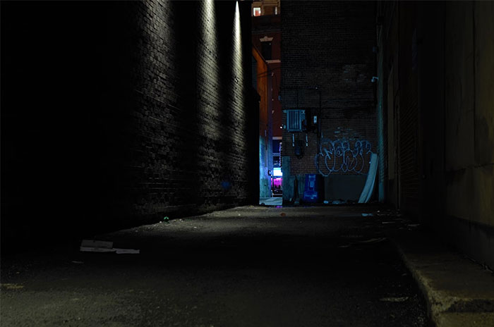 Dark urban alleyway at night, dimly lit, suggesting a creepy atmosphere.