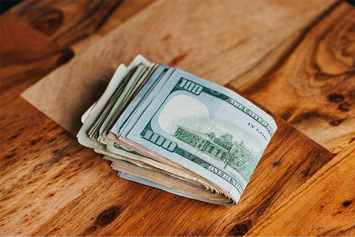 A stack of 100 dollar bills on a wooden table, related to dating challenges women face.