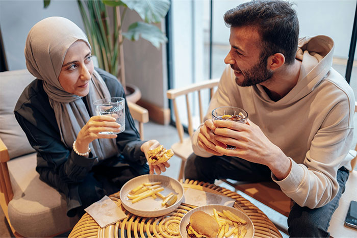 Woman and man enjoying a meal together, sharing conversation and smiles, holding drinks in a cozy dining setting.