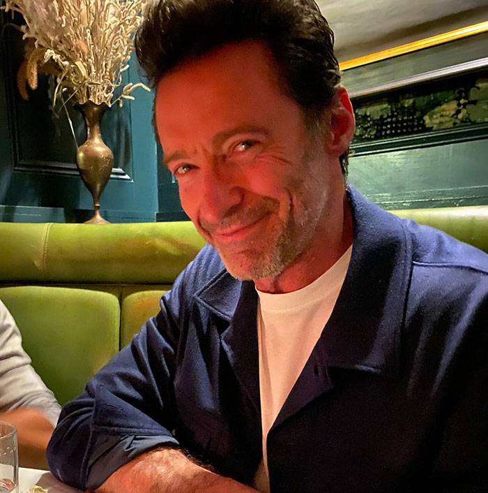 A man smiling at a restaurant, wearing a navy jacket, related to Hugh Jackman divorce news.