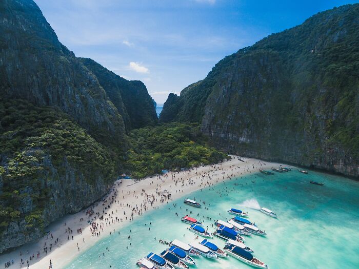 Beautiful beach with turquoise waters and boats, surrounded by cliffs, attracting many visitors. Stunning beaches.