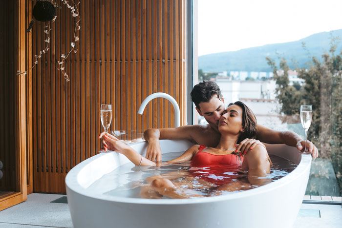 A couple in a bathtub, woman looks thoughtful while her partner embraces her; fat-shaming and anxiety context suggested. A couple in a bathtub, woman looks thoughtful while her partner embraces her; fat-shaming and anxiety context suggested.