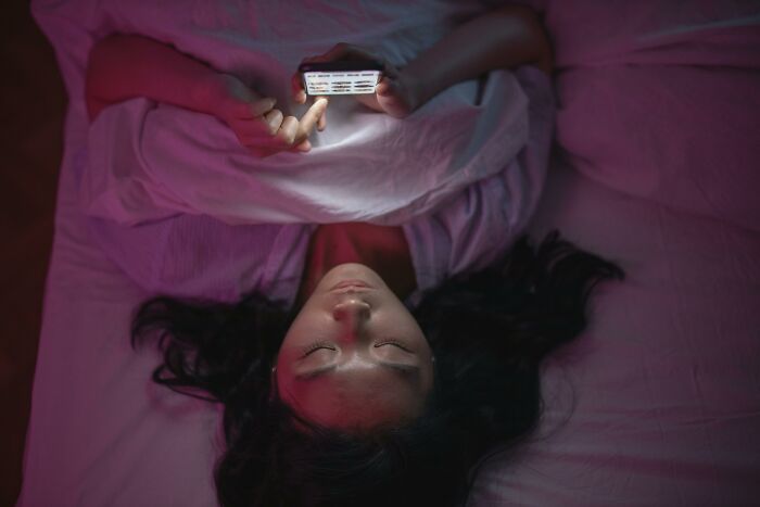 Woman lying in bed, looking at her phone intently, lit by the screen's glow, uncovering a sleepover secret. Woman lying in bed, looking at her phone intently, lit by the screen's glow, uncovering a sleepover secret.