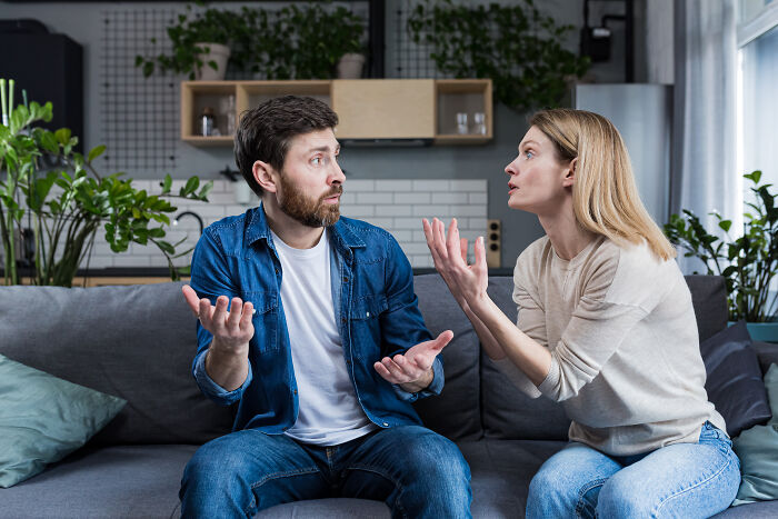Man and woman having a serious discussion on a sofa, highlighting parenting struggles.