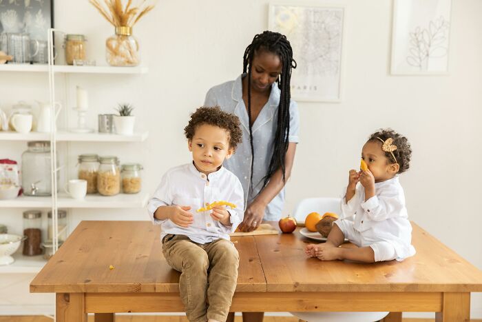 Mother with toddlers at a wooden table, highlighting parenting and family dynamics.