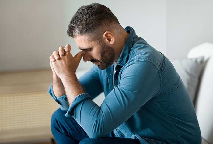 Man in a denim shirt sitting worried, hands clasped, reflecting on a prank incident.