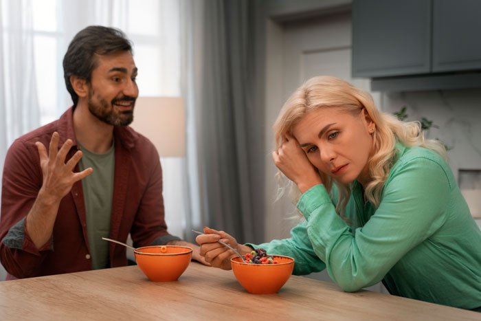 Man talking to a concerned woman at a table, with two bowls of fruit; concept related to husband, sister, pregnant wife.