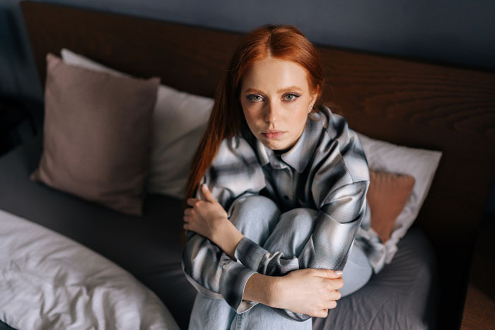 Woman with red hair sitting on a bed, looking thoughtful, related to husband sister pregnant wife theme.