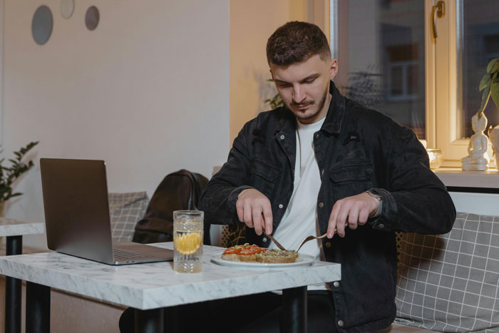 Man at cafe eating lunch with a laptop, spending money on meal and coffee.