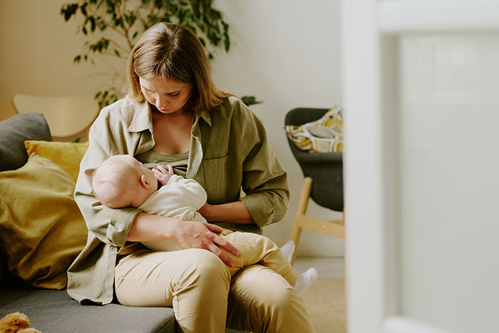 Mother holding newborn on couch, wearing casual clothing in a cozy living room. Mother holding newborn on couch, wearing casual clothing in a cozy living room.