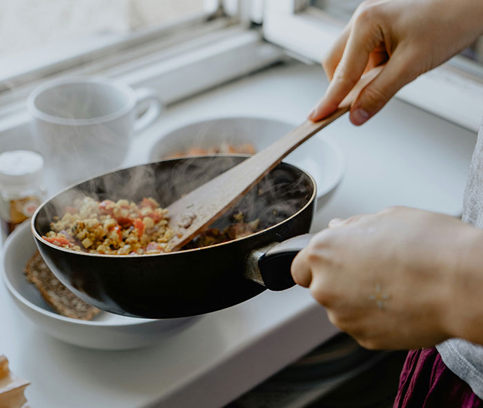 Person preparing lunch in a pan, emphasizing cooking and home meal preparation. Person preparing lunch in a pan, emphasizing cooking and home meal preparation.