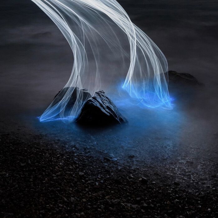 Drone-lighting captures rocks with ethereal blue light trails at night, showcasing stunning landscape photography.