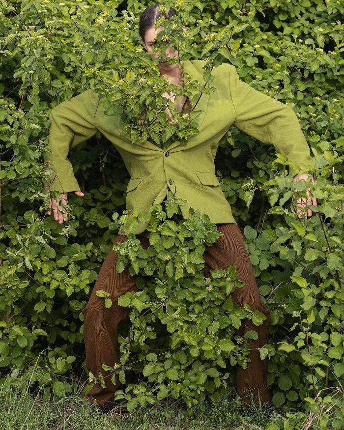 Solitary figure in a green suit blended into lush bushes, showcasing surreal photography by Ben Zank.