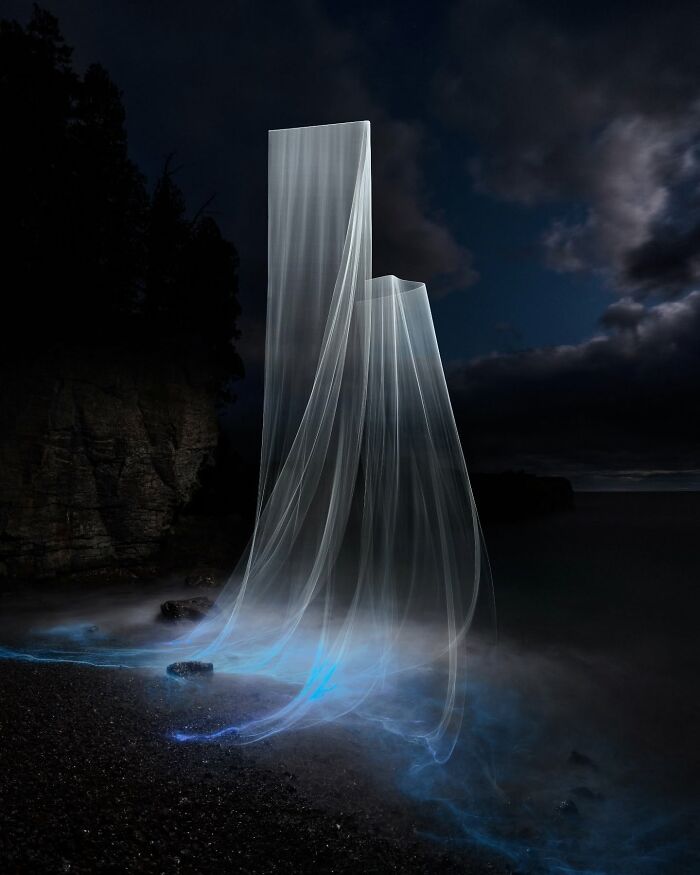 Drone lighting creates ethereal pillars in landscape photography scene with misty shores and cloudy sky.