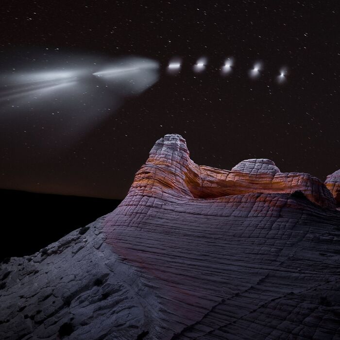 Drone-lit landscape at night, featuring rock formations under a starlit sky.