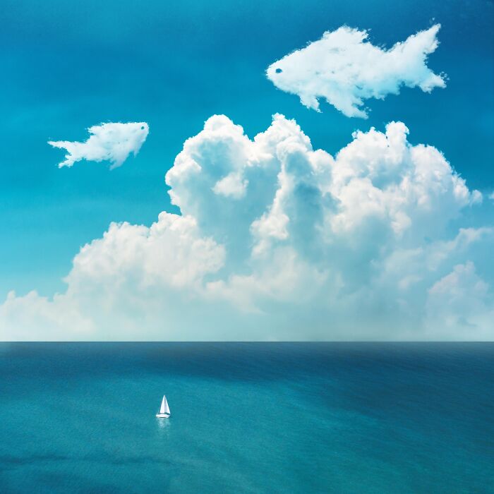 Surreal digital artwork of a sailboat on the ocean with fish-shaped clouds in a vivid blue sky.