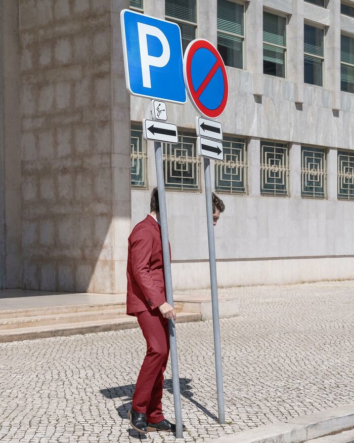 A person in a red suit stands behind two road signs, creating a surreal scene.