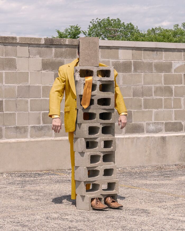 A person in a yellow suit obscured by cinder blocks, creating a surreal landscape scene.