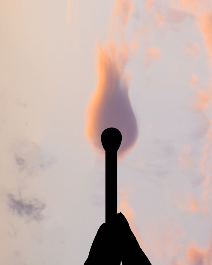 Silhouette photography of a hand holding a matchstick against a pastel sky.