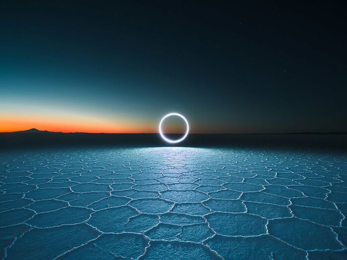 Drone-lit circle over hexagonal salt flats at sunset.