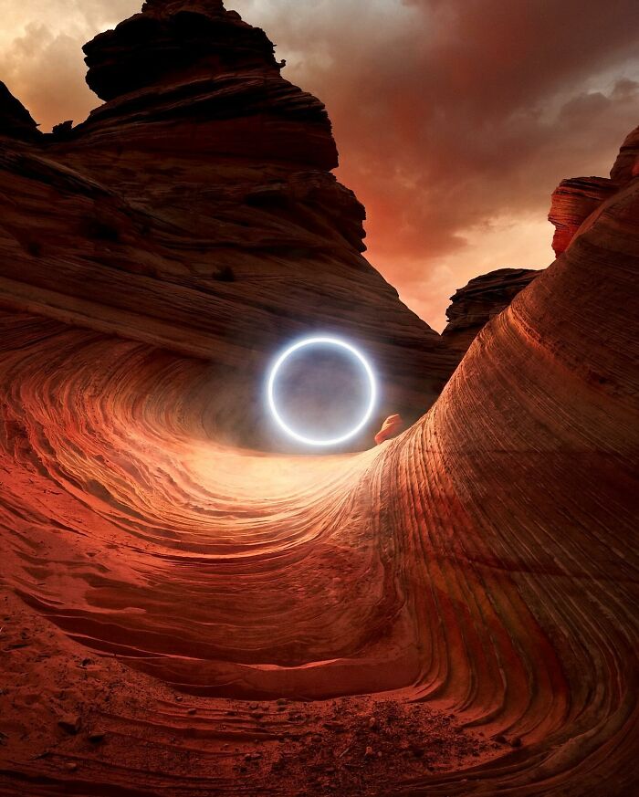 Drone-lit landscape with glowing circle against red rock formations at sunset.