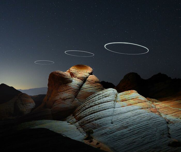 Drone-lighting landscape photography with illuminated rock formations and circular light trails in the night sky.