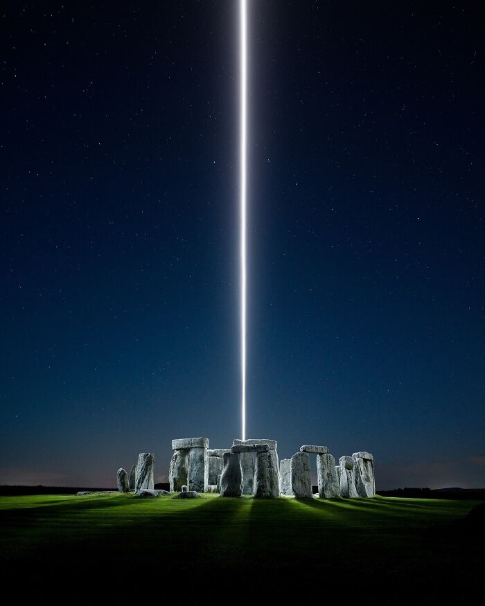 Drone lighting creates a vertical beam over Stonehenge at night, showcasing landscape photography by Reuben Wu.