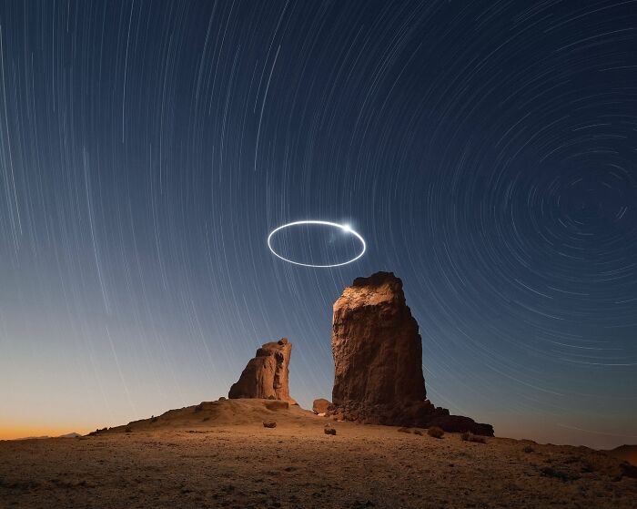 Drone-lighting landscape photography featuring dramatic rocks under a star-streaked night sky.