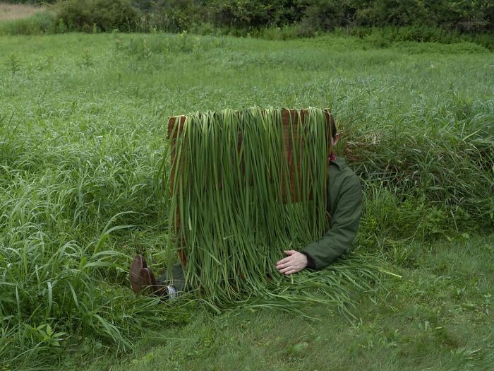 Person hidden in tall grass with legs out, creating a surreal landscape scene.