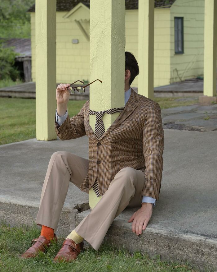 A surreal photograph by Ben Zank showing a solitary figure in a suit sitting behind a pole holding glasses.