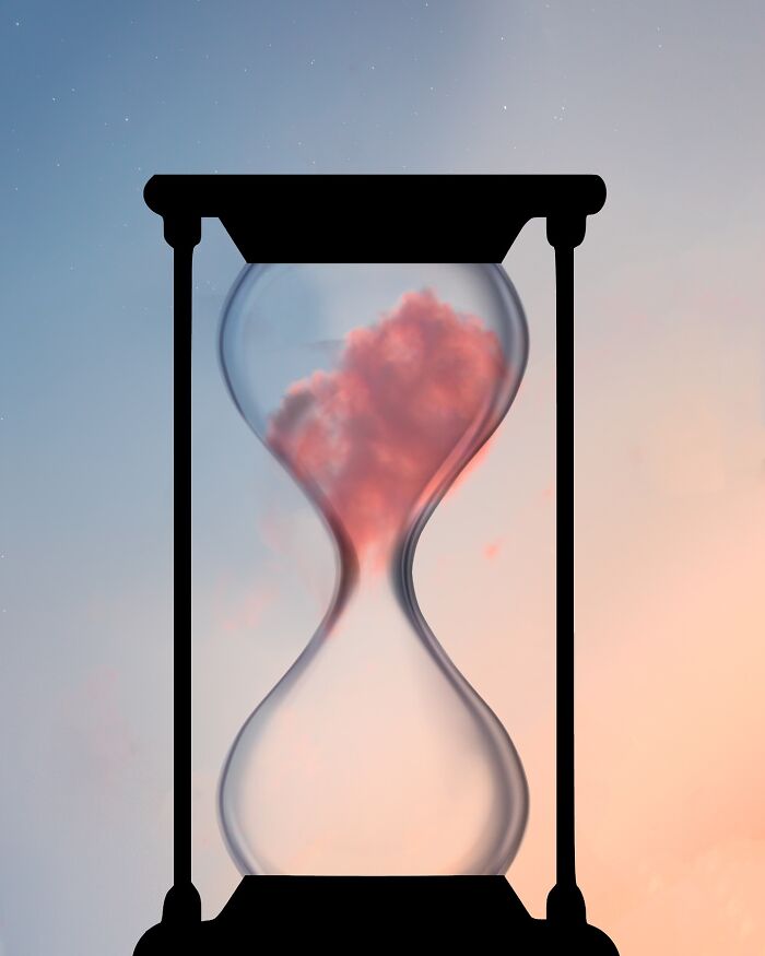 Silhouette photography of an hourglass with a pink cloud inside against a pastel sky by Lân Nguyen.