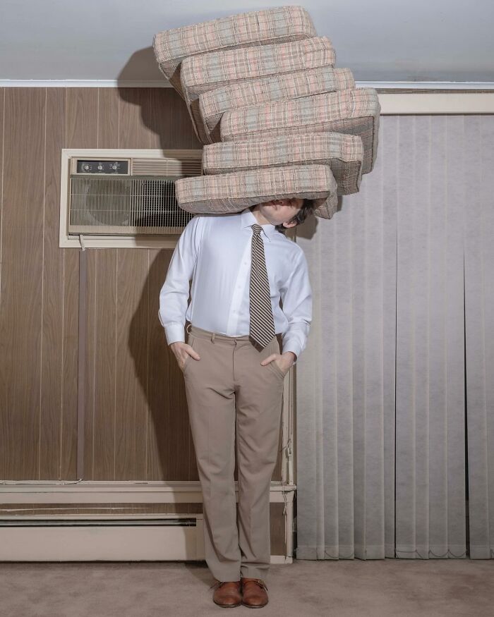 Solitary figure in surreal pose with stack of cushions obscuring head in a vintage room.