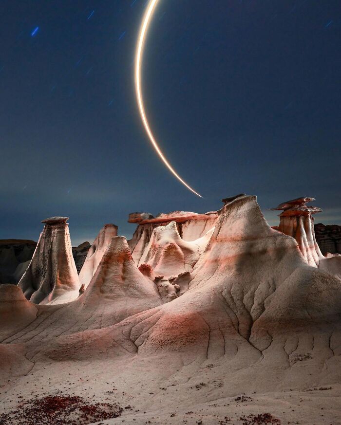 Drone-lighting enhances desert landscape formations under starry sky.