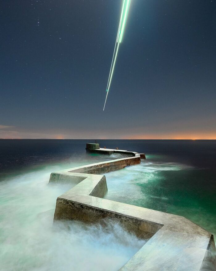 Drone-lit seascape with geometric pier under a night sky, featuring Reuben Wu's landscape photography.