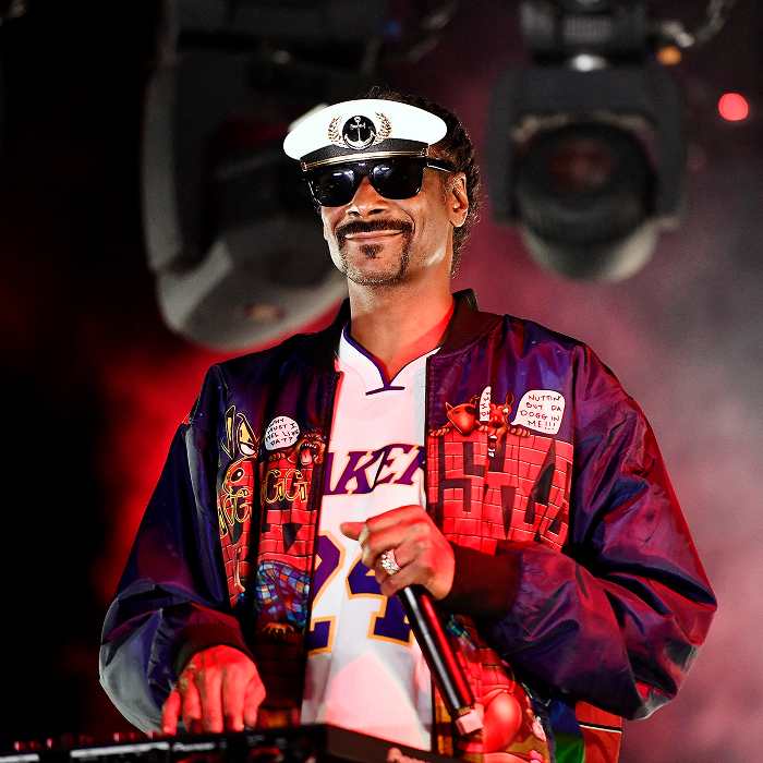 "Snoop Dogg on stage in vibrant jacket and cap, performing under colorful lights.