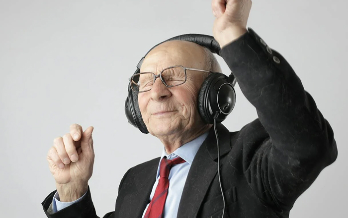 Elderly man joyfully dancing, wearing headphones and a suit, exemplifying genius ways to entertain yourself.