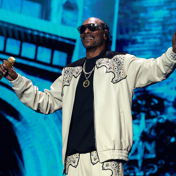 Snoop Dogg performing on stage in a stylish outfit, holding a microphone, illustrating net-worth success through music and business.
