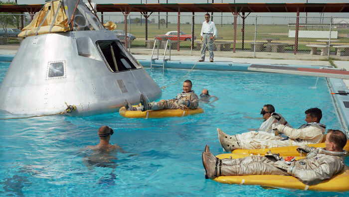 Astronauts in training suits floating beside a capsule in a pool, part of a creepy photo collection with dark histories.